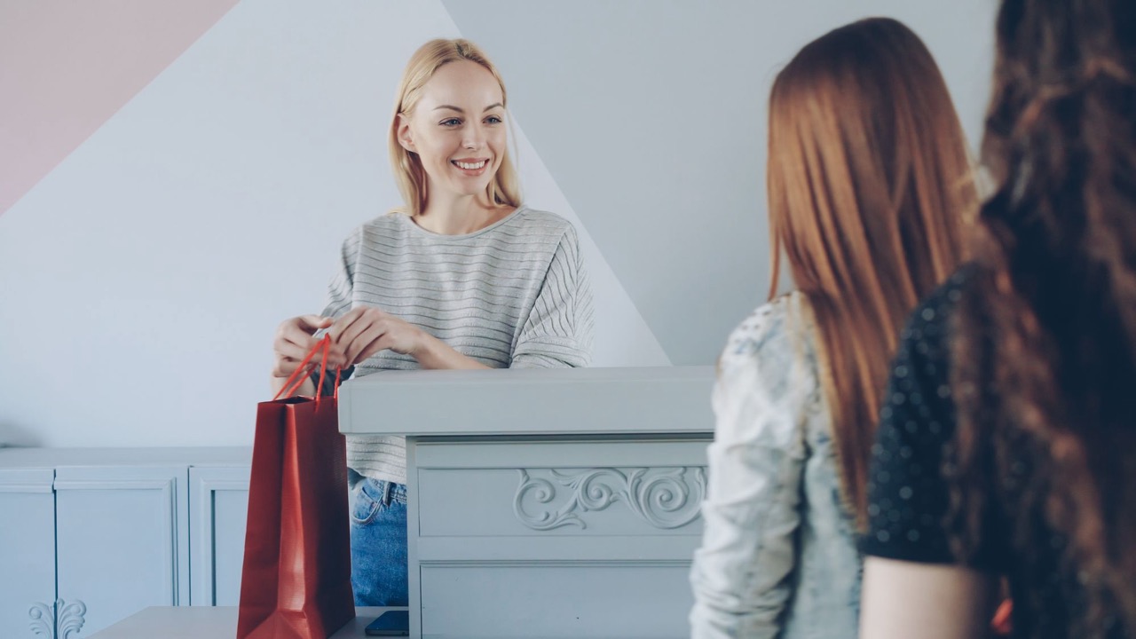 A local shop employee handing a finished purchase to customers.