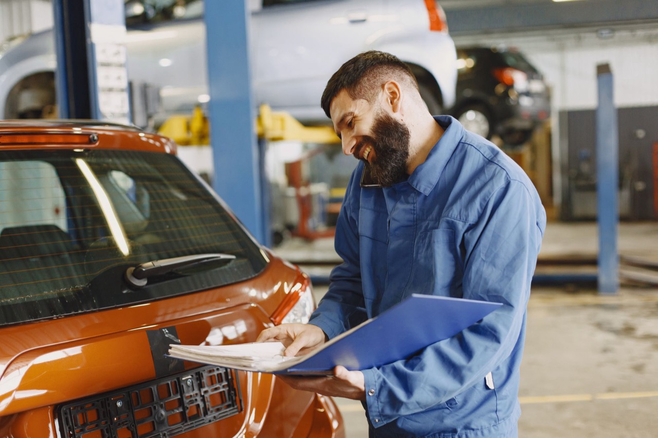 An auto mechanic answering his phone while working beside a car.
